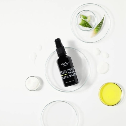 Matowy czarny flakon z kremem do twarzy Veoli Botanica CERAMIDE SKIN BARRIER na białym tle, otoczony szkłem z aloesem i kolorowymi substancjami, widok z góry podkreśla estetykę produktu.