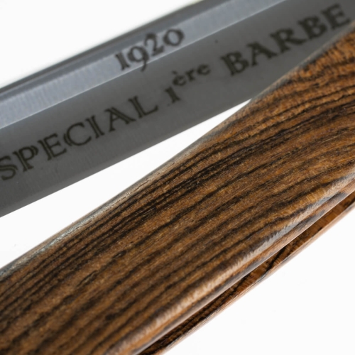 Brzytwa do golenia z drewnianym uchwytem bocote o naturalnych słojach, ostrze z logo SPECIAL ière BARBE i datą 1920, matowe stalowe wykończenie, zbliżenie podkreślające szczegóły.