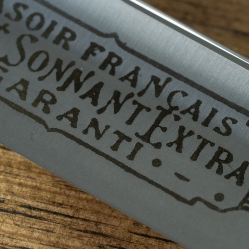 Brzytwa Thiers Issard Evide Sonnant Extre z widocznym logo i napisem Sonnant Extra na metalowej powierzchni. Zbliżenie na fakturę ostrza w srebrnym kolorze, na tle drewnianego blatu.