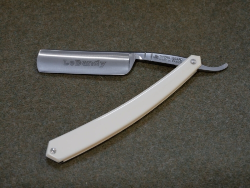 Brzytwa Thiers Issard Le Dandy White 5/8 z ergonomiczną białą rączką i metalowym ostrzem z napisem Le Dandy, ułożona poziomo na szarym tle, ukazująca detale i charakterystyczny kształt.