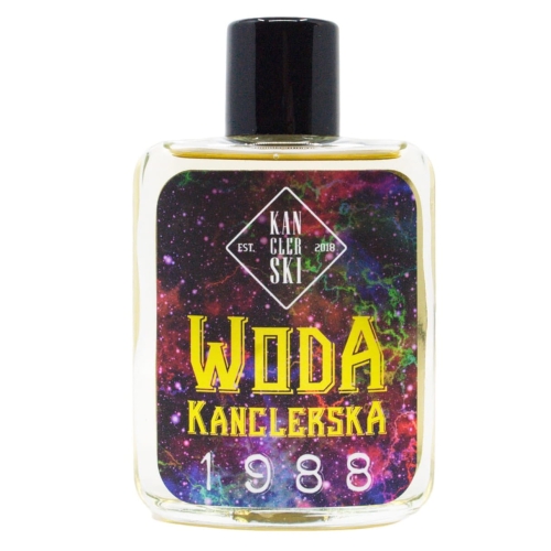Woda po goleniu Kanclerska 1988 w przezroczystej, prostokątnej butelce z czarnym korkiem. Etykieta fioletowo-niebiesko-czarna z dużymi złotymi literami „WODA KANCLERSKA” i rokiem 1988. Butelka stoi na białym tle.