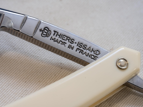 Brzytwa Thiers Issard ze stali szlachetnej z kościaną rękojeścią. Widoczne napisy THIERS-ISSARD MADE IN FRANCE i teksturowany brzeg ostrza na jasnym tle.
