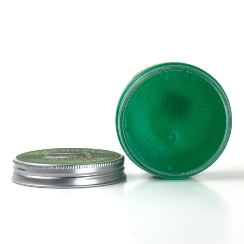 Pomada do włosów Lockhart's Goon Grease 96g w przezroczystym słoiku z metaliczną pokrywką i zielonym logo, częściowo otwarta, ukazująca intensywnie zieloną pomadę. Białe tło podkreśla kolor produktu.