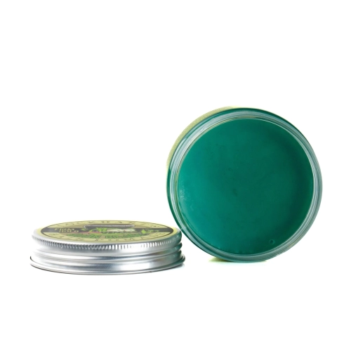 Woskowa pomada do włosów Lockhart's Goon Grease w metalowym słoiku, widoczna z boku, częściowo otwarta. Zielony produkt wewnątrz słoika, z kolorową etykietą na wierzchu, która zawiera grafikę i napis. Słoik ma gładką powierzchnię i wyprofilowaną krawędź.