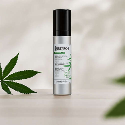 Masaż do twarzy i brody Bullfrog, 75 ml, z metalowym pojemnikiem w kolorze srebrnym. Produkt z czarną nakrętką, z etykietą z zielonymi detalami. Opis zawiera nazwy w kilku językach. Maska przeciwstresowa umieszczona na jasnym tle, obok liści konopi.