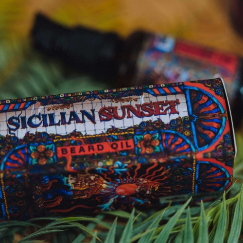 Olejek do brody w butelce 30 ml z kolorową etykietą przedstawiającą motywy w stylu sycylijskim, w tym napis SICILIAN SUNSET oraz BEARD OIL. Produkt leży na zielonym tle liści palmowych, w zbliżeniu ukazujące detale etykiety i tekstury.