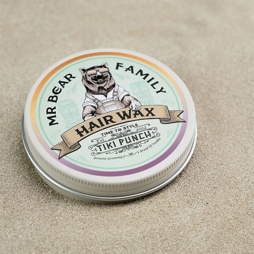 Metalowa puszka wosku do włosów Mr Bear Family Tiki Punch, ok. 10 cm, z kolorowym wzorem misia w okularach i napisem „HAIR WAX” na beżowym tle, ustawiona na piasku pod kątem pokazując logo i etykietę.