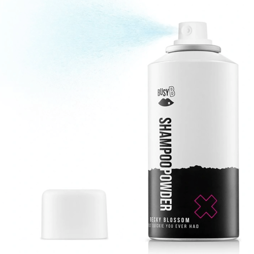 Suchy szampon Becky Blossom 150 ml w białej metalowej butelce z czarnymi i różowymi detalami, z napisem SHAMPOO POWDER i logo BUSY B, obok biały korek, w tle rozpryskujący się niebieski spray.