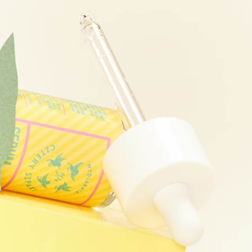 Serum na końcówki w przezroczystej buteleczce z białą pipetą, etykieta w kolorze żółtym z różowymi napisami i zielonymi grafikami. Produkt leży na jasnym tle, widoczny jest szczegółowy wzór na etykiecie.