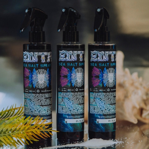 Sól morska RareCraft 250 ml w czarnej butelce z etykietą ozdobioną niebiesko-fioletowym wzorem, logo i gotyckimi napisami. Butelki na lustrzanym tle z solą i koralem w tle.