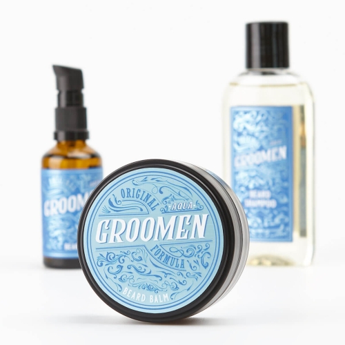 Zestaw do pielęgnacji brody Aqua Groomen: matowy słoiczek z błękitną etykietą Beard Balm, butelka z brązowego szkła i pastelowe opakowanie z logo Groomen, ustawione na białym tle, słoiczek leży.