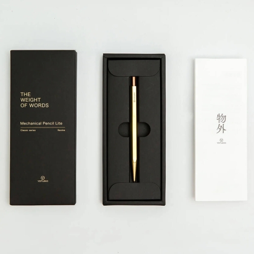 Ołówek mechaniczny YSTUDIO Classic Revolve Lite mosiężny w czarnej kasetce z złotymi napisami THE WEIGHT OF WORDS i Mechanical Pencil Lite. Obok biały składany ulotek z logo YSTUDIO na jednolitym tle.