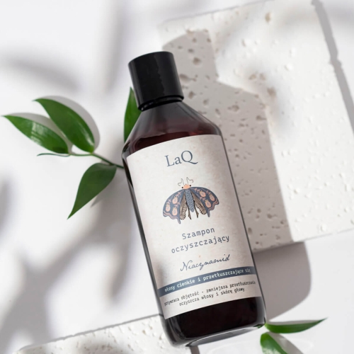 LaQ szampon oczyszczający Niacynamid 300 ml, w ciemnej butelce z etykietą motyla i napisem, na białym tle. W tle zielone liście sugerujące naturalny skład.