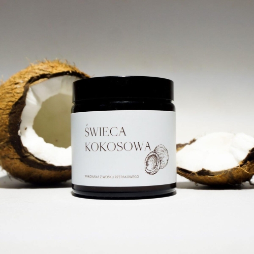 Świeca kokosowa z wosku rzepakowego 120 ml w czarnej, cylindrycznej słoiczku z czytelną etykietą. Ujęcie frontalne, z widocznym fragmentem łupiny kokosa w tle. Prosty, jasny kontekst, podkreślający naturalne materiały.