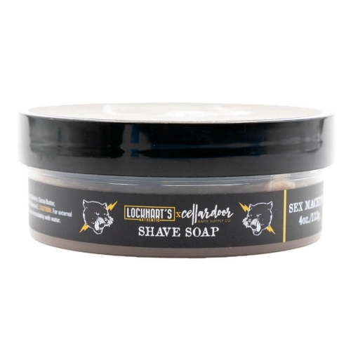 Mydło Lockhart's do golenia w czarnej puszce z przezroczystym wieczkiem. Etykieta z napisami SHAVE SOAP i SEX MACHINE oraz logo kota. Puszka leży poziomo, podkreślając szczegóły i kolory.