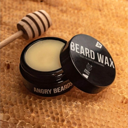 Czarny słoik z woskiem do brody i wąsów Angry Beards, otwarty, z widocznym żółtawym wnętrzem. Na wieczku napis BEARD WAX oraz logo marki. Tło z naturalnego plastra miodu, co podkreśla naturalny charakter produktu.