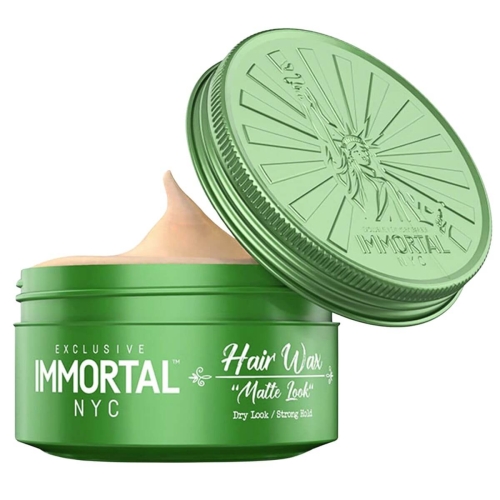 Matowa pomada do włosów w zielonym opakowaniu z metalową zakrętką, otwarte wieczko z detalem Statuy Wolności i napisami: EXCLUSIVE IMMORTAL NYC oraz Hair Wax Matte Look. Kremowa konsystencja na jasnym tle.