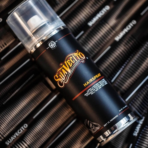 Lakier do włosów Suavecito 283 ml w czarnej butelce z metalowym korkiem, logo na wieczku, napis HAIRSPRAY i informacja o długotrwałym utrzymaniu fryzury, na tle z czarnymi grzebieniami.