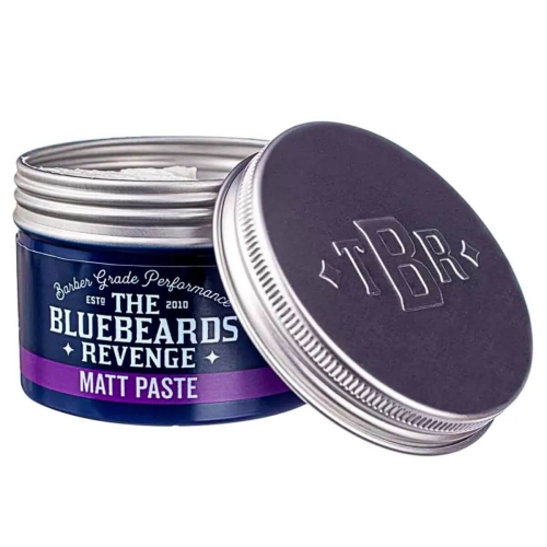 Matowa pasta do stylizacji włosów w metalowym, ciemnoniebieskim słoiku z lekko uchyloną, ciemnoszarą pokrywką z logo TBR. Etykieta: The Bluebeards Revenge Matt Paste i Barker Grade Performance.