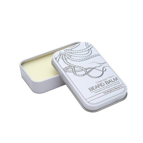 Biały metalowy pojemnik z otwartym wieczkiem, zawiera żółty balsam do brody z napisem Creampot Tom's BEARD BALM i grafiką na wieczku.