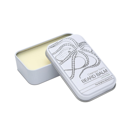 Biała metalowa puszka z otwartym balsamem do brody o jasnej konsystencji. Na wieczku czarny motyw ośmiornicy, napis CREAMPOT TOM'S BEARD BALM oraz zapach Lime & Basil. Proste tło podkreśla elegancję.