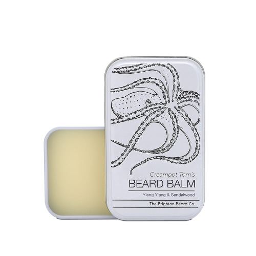 Biały metalowy pojemnik z balsamem do brody o kremowym kolorze, częściowo otwarty. Na froncie czarny nadruk ośmiornicy i napis Creampot Tom's BEARD BALM pod rysunkiem.