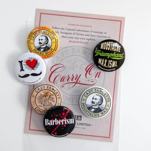 Zestaw przypinek na białym tle: czarna z napisem MOUSTACHE Triumphant WAX 15ML, biała z czerwonym sercem i wąsami, brązowa i złota z logo CAPT FAWCETT, czarna Barberism, srebrna z wizerunkiem mężczyzny. Tło z logo Carry On.