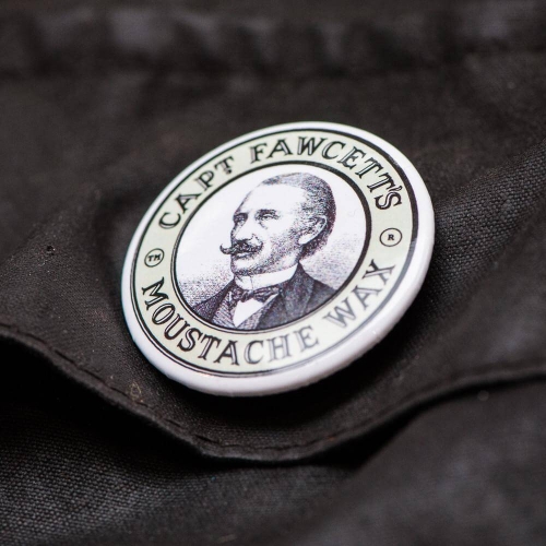 Biały okrągły zegarek z czarnym nadrukiem mężczyzny w garniturze i napisem CAPT FAWCETT'S MOUSTACHE WAX na czarnym tle materiału.