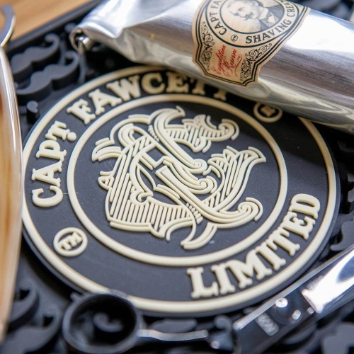 Logo Capt. Fawcett na czarnym tle z białym napisem CAPT. FAWCETT LIMITED. Obok metalowa tubka kremu do golenia z etykietą. Całość na jasnym tle z drewnianym akcentem.