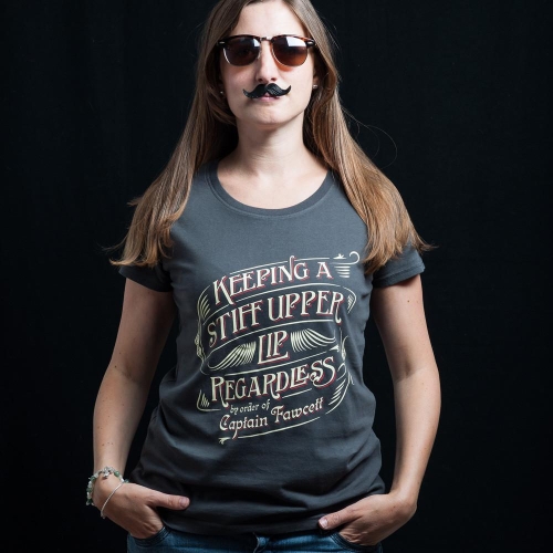 Szary t-shirt z okrągłym dekoltem i czerwono-złotym napisem KEEPING A STIFF UPPER LIP REGARDLESS by order of Captain Fawcett. Modelka z długimi włosami, okularami przeciwsłonecznymi i sztucznym wąsem, stoi na czarnym tle.