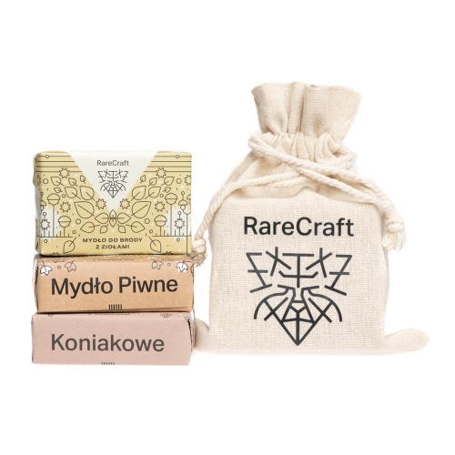Zestaw 3 mydeł RareCraft w jasnej torbie z logo: mydło do brody ziołowe, piwne w brązowym i koniakowe w różowym opakowaniu, ułożone jedno na drugim na jednolitym tle.
