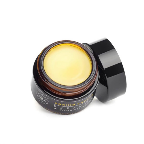 Mały brązowy słoik z perfumami waniliowymi, czarna zakręcana pokrywka, kremowy przezroczysty wosk w środku, etykieta vanilla vanilla z informacją o woskach pszczelich, otwarte wieczko, na białym tle.