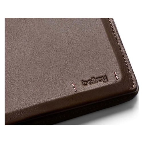 Skórzany, ciemnobrązowy portfel z logo bellroy i jasną dekoracją z nitów. Zbliżenie na krawędź, lekko otwarty, ukazujący wysoką jakość i staranne wykonanie.