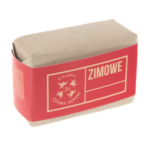 Błotnisty kawałek mydła w kostce w kartonowym opakowaniu. Szersza krawędź z widoczną czerwoną etykietą z napisem „ZIMOWE” oraz logo producenta „Mydlarnia Cztery Szpaki”. Opakowanie ma matową fakturę i jest lekko otwarte.